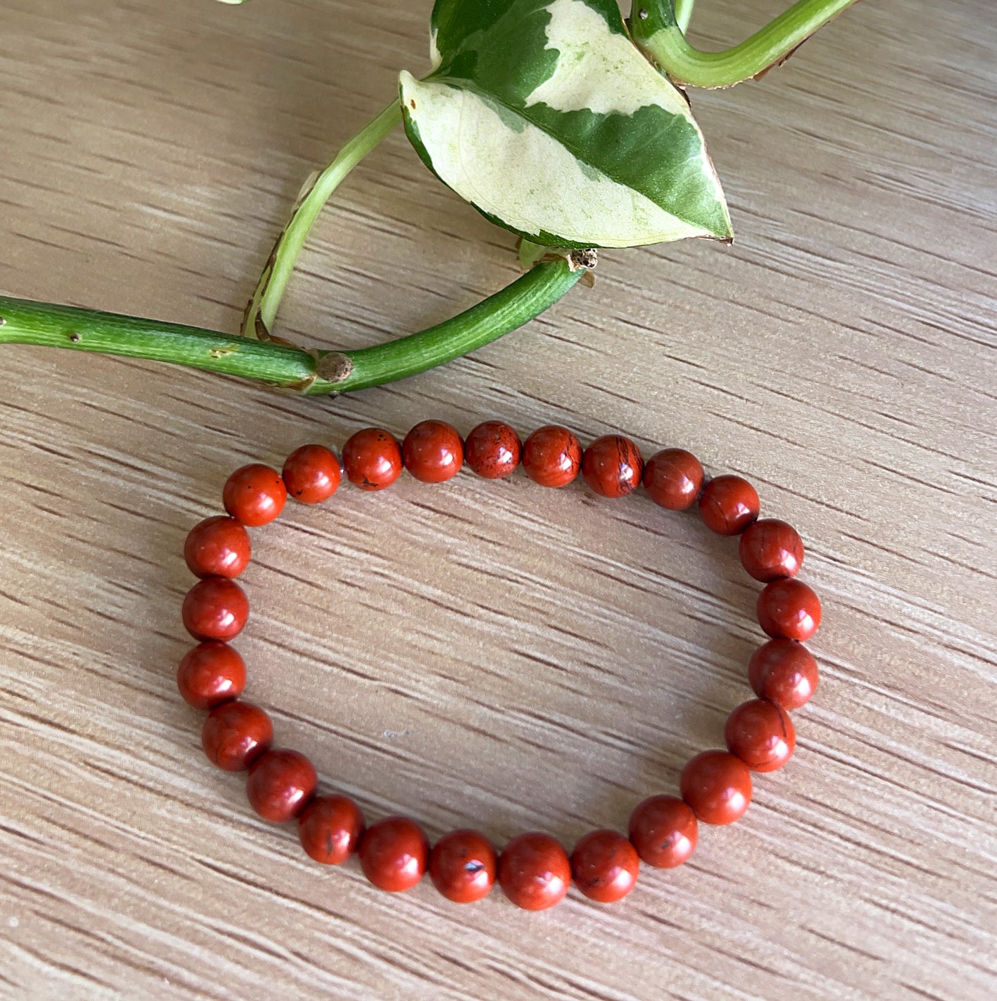 Red Jasper beaded bracelet on a wooden surface with green leaves in the background
