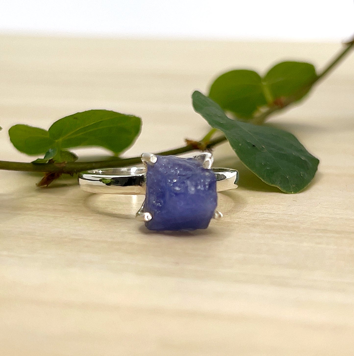 Silver ring with Tanzanite on a beige surface with green leaves.
