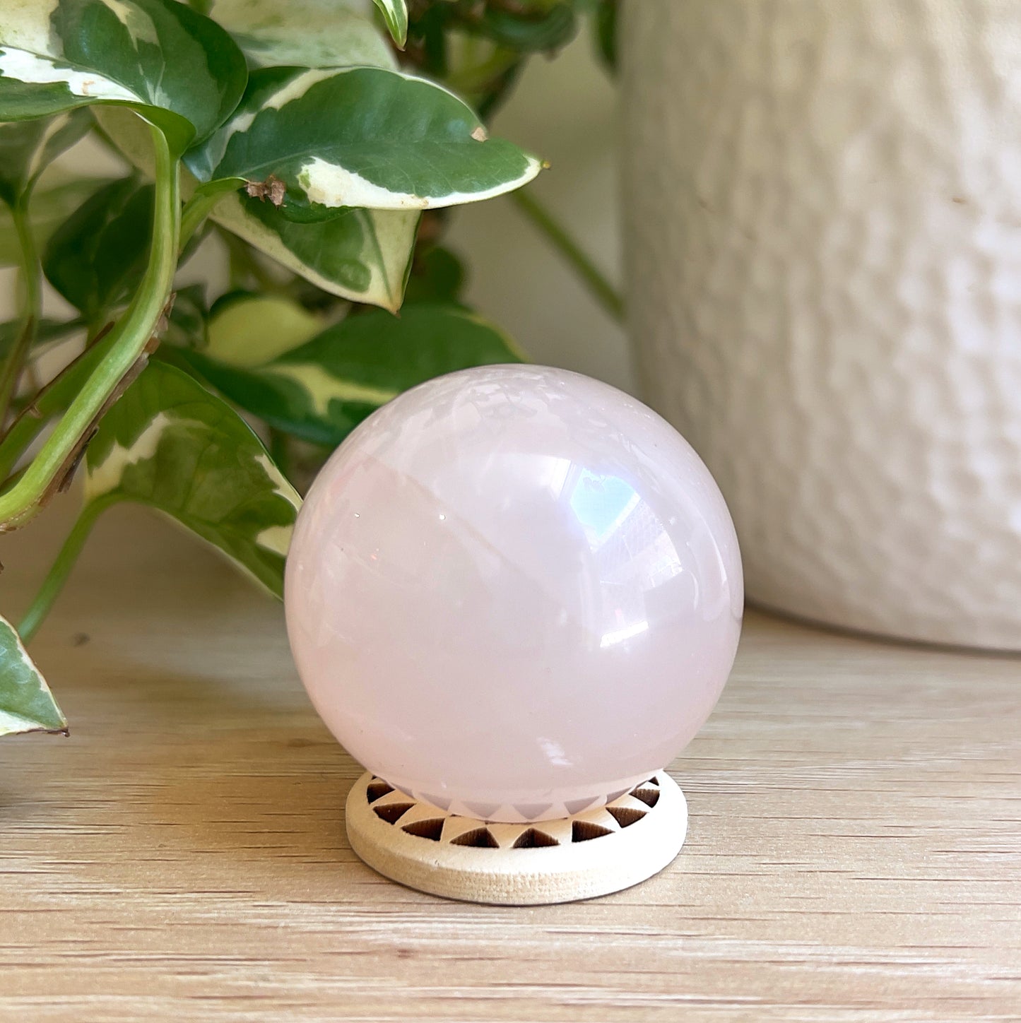 Rose quartz sphere on wooden stand with plant in background