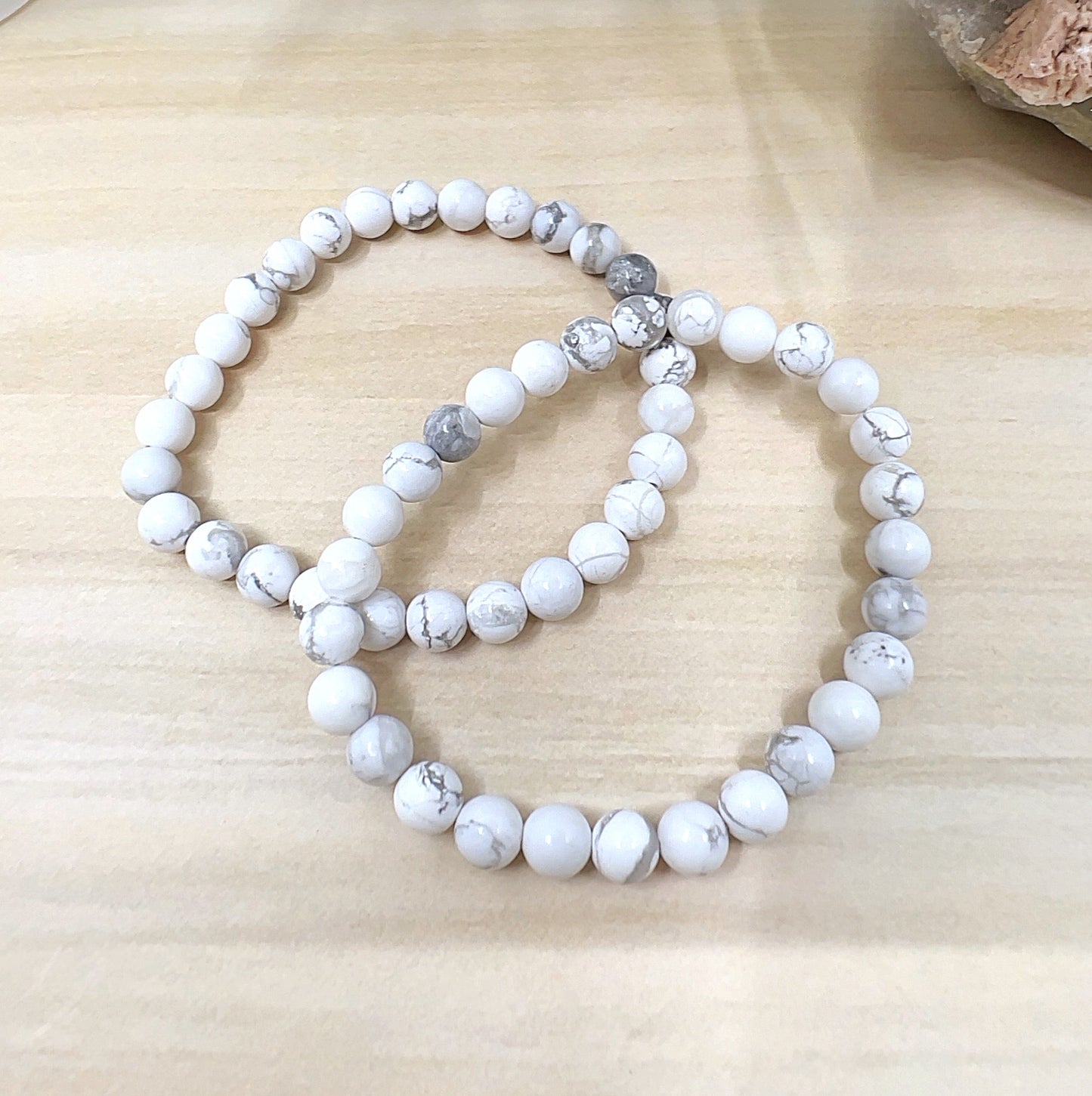 Handmade White Howlite crystal bead bracelet with 6mm round beads on stretchy cord, featuring smooth white stones with natural grey veining, displayed on a wooden surface. | Simply Esoteric
