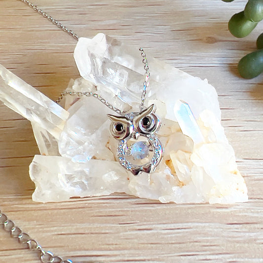 Sterling silver owl-shaped pendant featuring an Australian white opal at its centre, accented with cubic zirconia, displayed on a cluster of clear quartz crystals with a wooden background and greenery. | Simply Esoteric