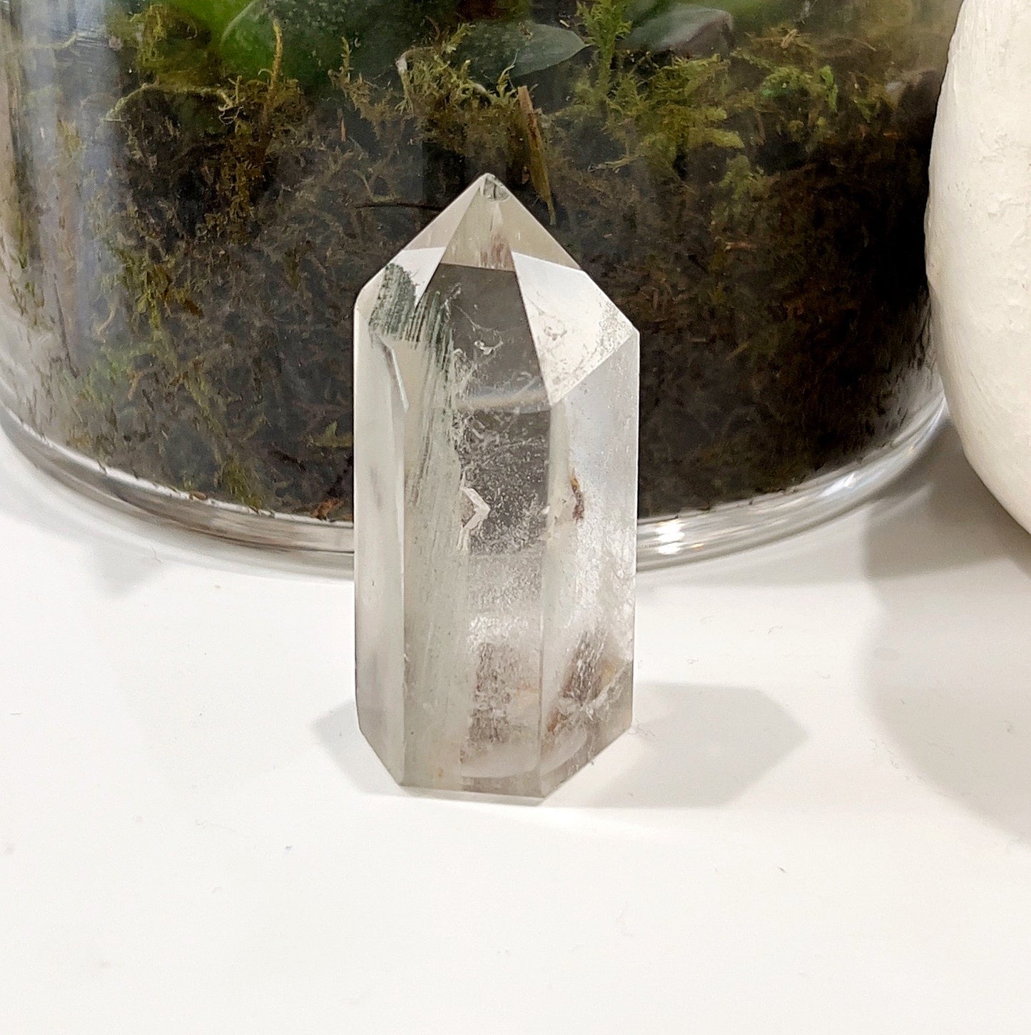 Phantom Quartz Tower measuring approximately 5.5cm, featuring unique phantom inclusions, set against a background with a glass pot containing a succulent plant. | Simply Esoteric