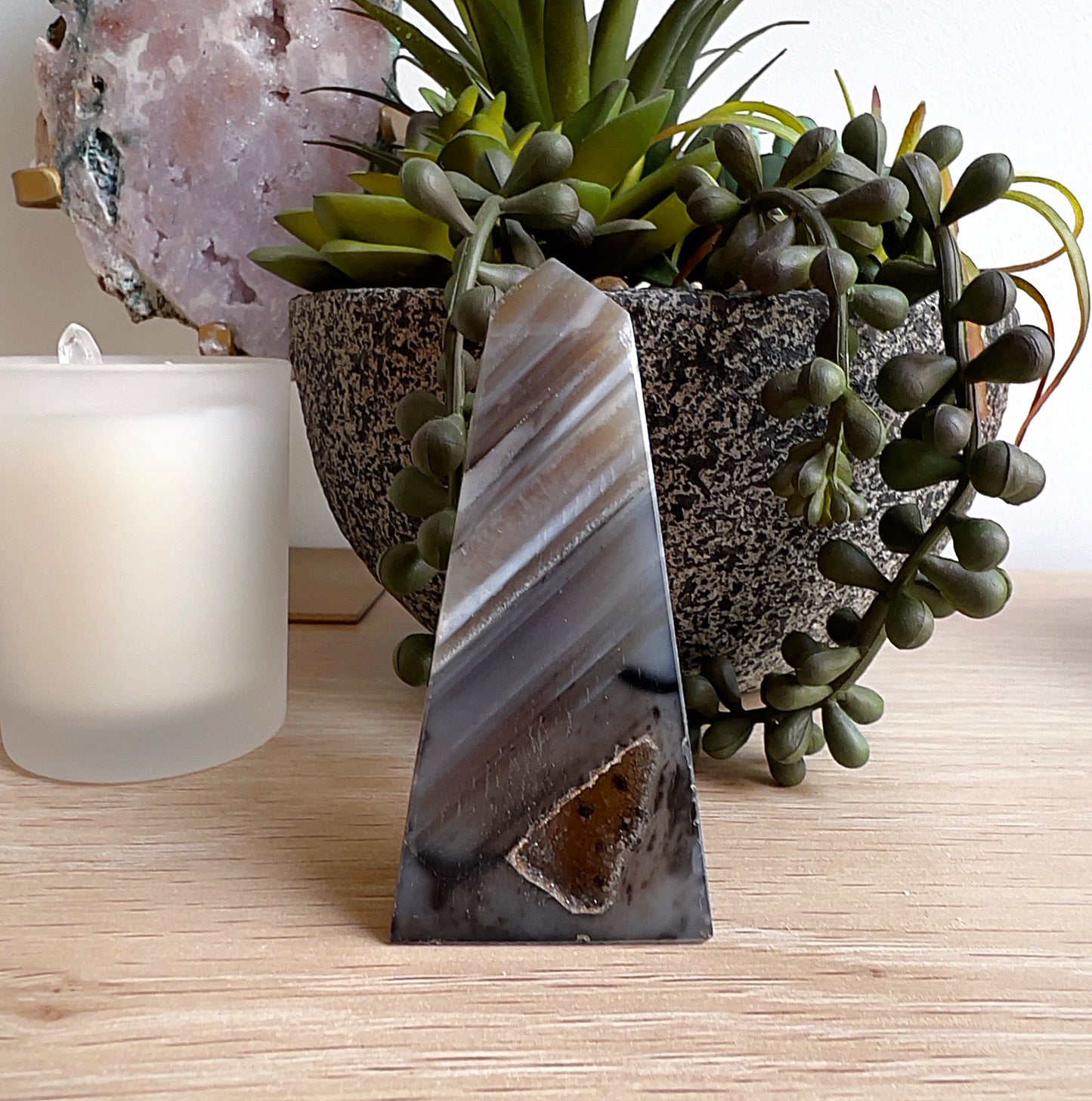 Brown agate obelisk crystal standing upright on a wooden surface, displaying layered natural brown and grey banding with a geode-like pocket at the base. | Simply Esoteric