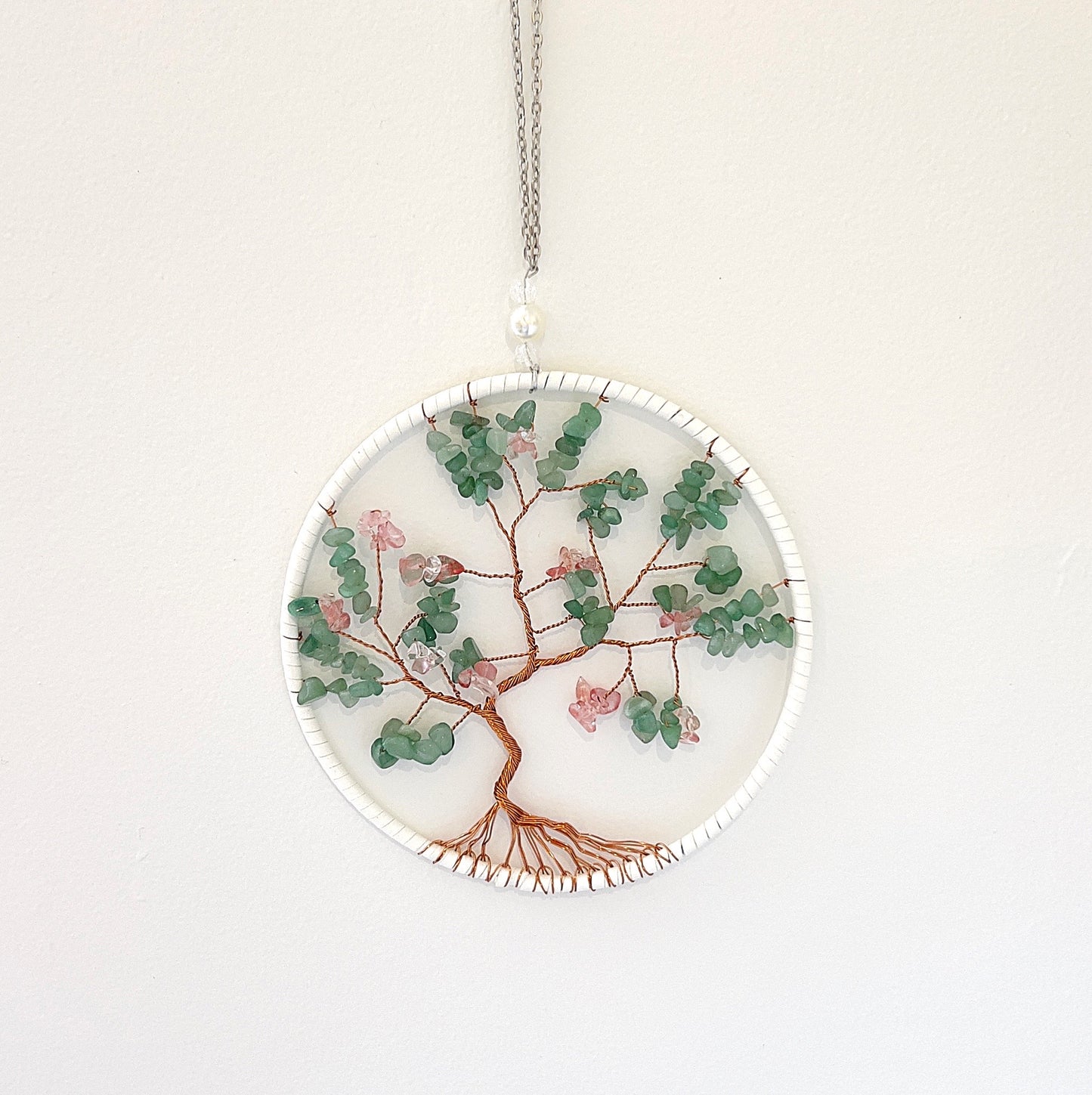 A green aventurine wire wrap wall decoration featuring a tree of life design. The decoration is approximately 20cm in diameter, with vibrant green aventurine chips intricately wrapped in copper wire, suspended in a circular metal frame. The piece is displayed against a white background, highlighting its natural beauty and detailed craftsmanship. | Simply Esoteric