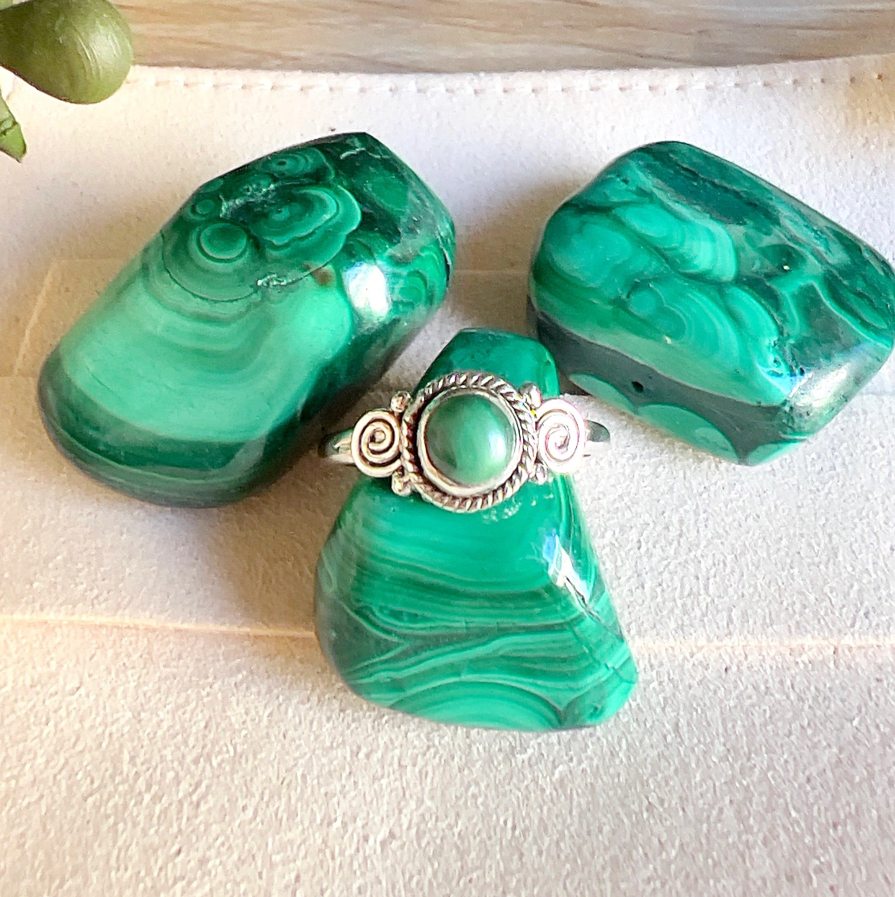 Sterling silver Malachite ring with round green stone and decorative swirl detailing, displayed with polished Malachite crystals on a light surface. | Simply Esoteric