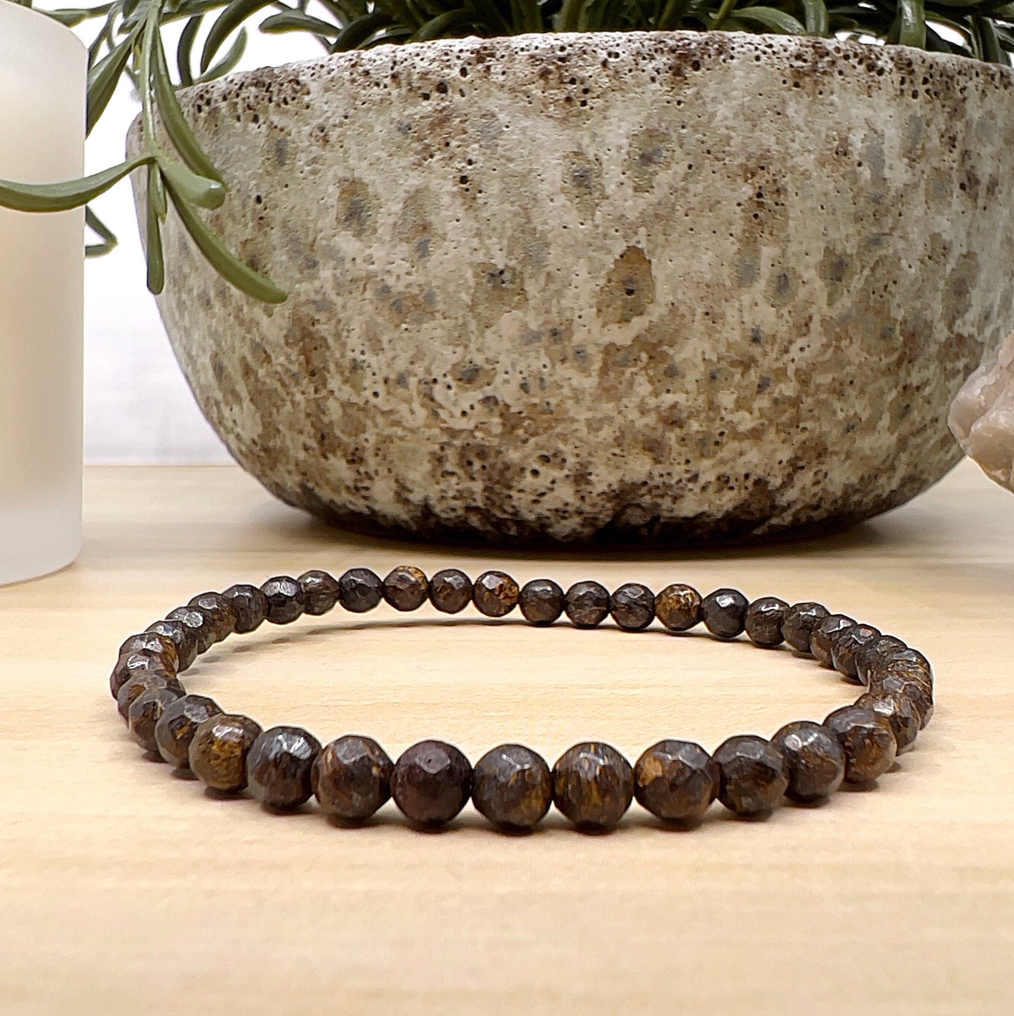 Handmade Bronzite faceted bead bracelet with 4mm round beads on stretchy cord, featuring earthy brown stones with golden-bronze shimmer, displayed on a wooden surface. | Simply Eosteric