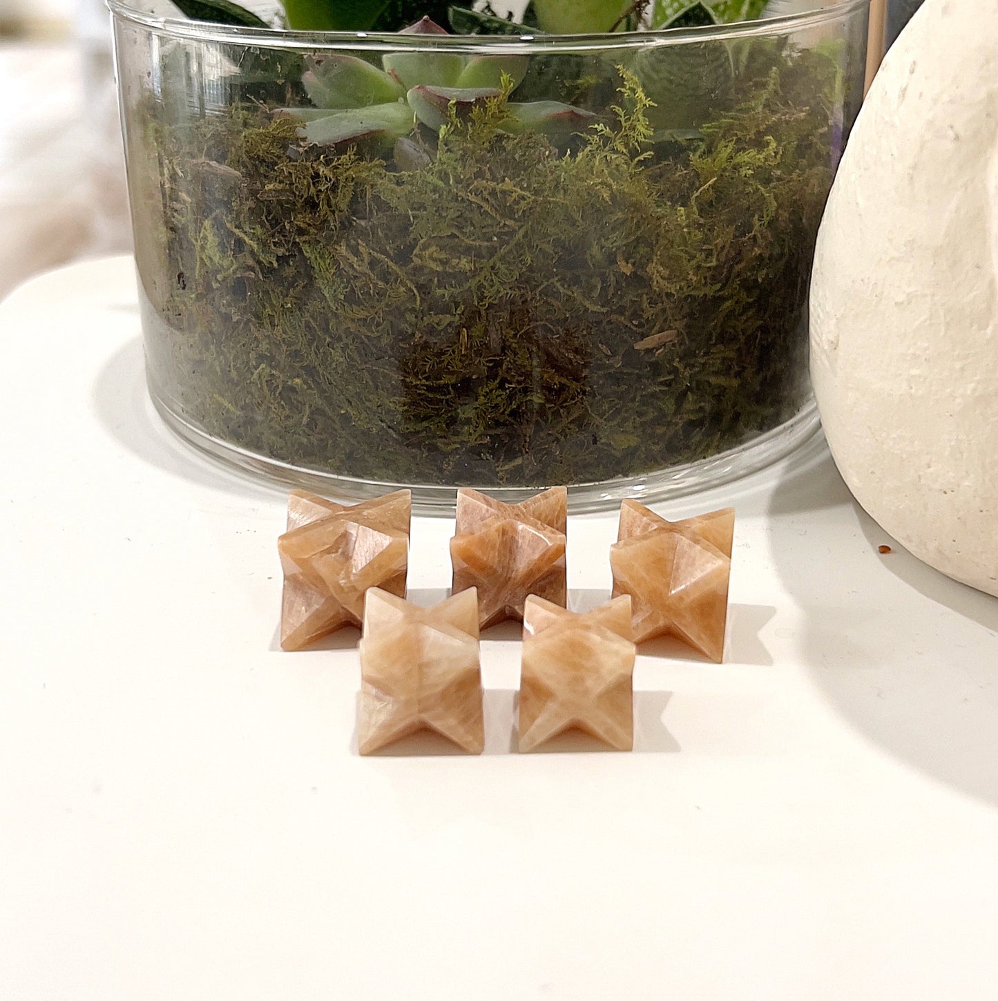 Set of six Orange Moonstone Merkaba Stars, each approximately 2-2.5cm in size, displayed in front of a plant with lush green moss. | Simply Esoteric
