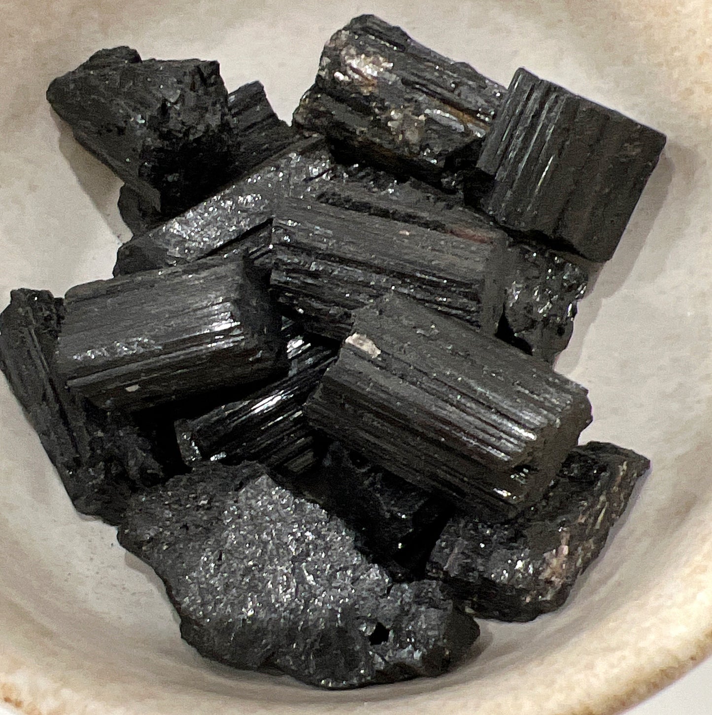 A collection of raw Black Tourmaline pieces in a bowl, showcasing their rugged, natural appearance and deep black color with shiny surfaces. | Simply Esoteric