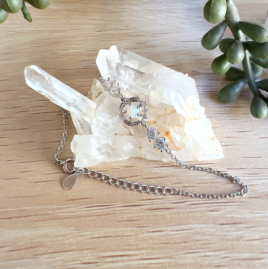 Sterling silver bracelet featuring a central Australian white opal set in a feather-inspired design with cubic zirconia accents, displayed on a cluster of clear quartz crystals on a wooden surface. | Simply Esoteric