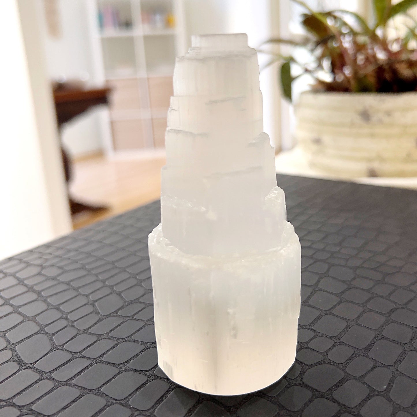 A selenite tower standing upright with a smooth, polished surface that glows with a pearlescent sheen. The tower's translucency and fine striations catch and diffuse light, giving it an ethereal appearance that embodies purity and calm. | Simply Esoteric