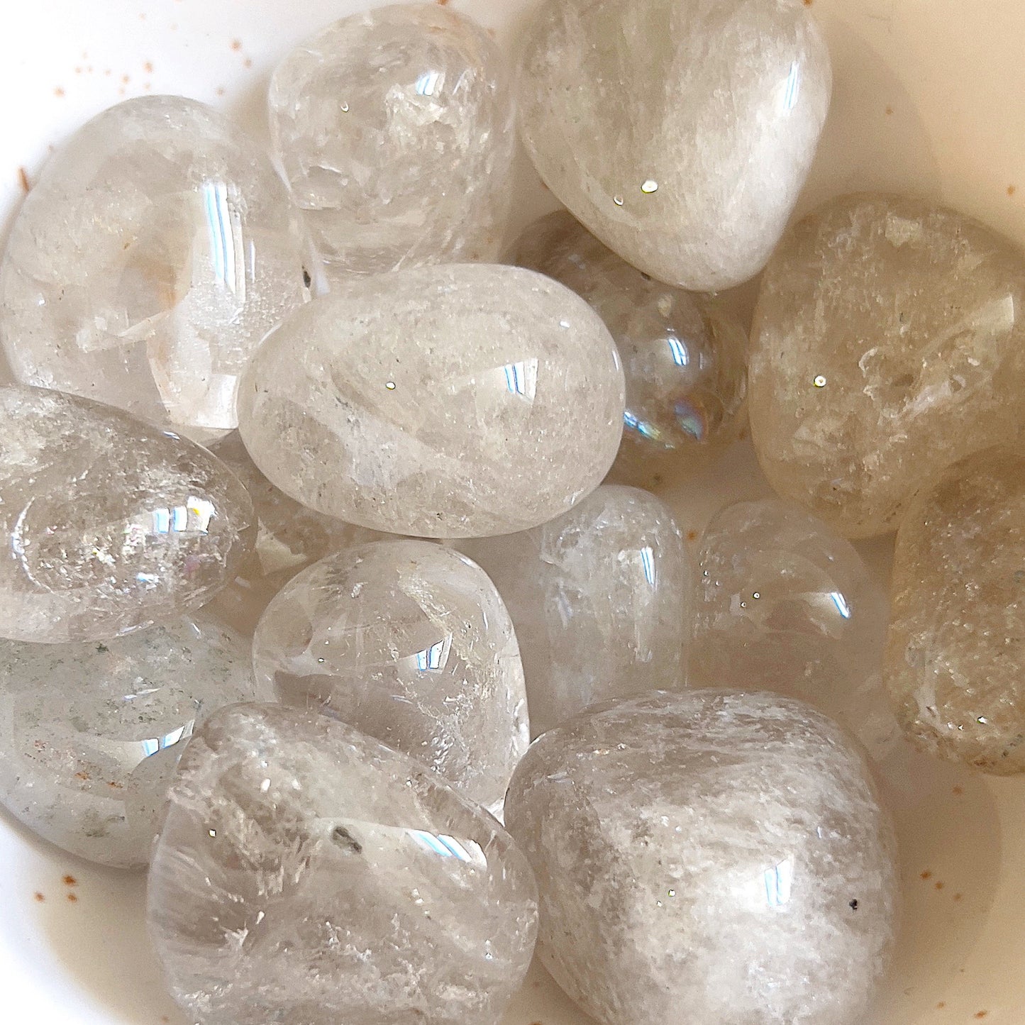 A collection of smokey quartz tumbled stones clustered together, their translucent, misty surfaces ranging from light to dark shades of gray and brown. The stones shimmer with a subtle brilliance, revealing faint natural inclusions and a smooth, polished texture that conveys a sense of calm strength. | Simply Esoteric