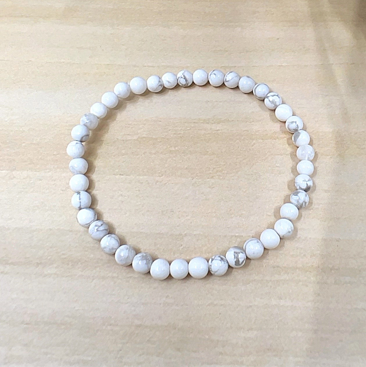 Handmade White Howlite crystal bead bracelet with 4mm round beads on stretchy cord, featuring smooth white stones with natural grey veining, displayed on a wooden surface. | Simply Esoteric