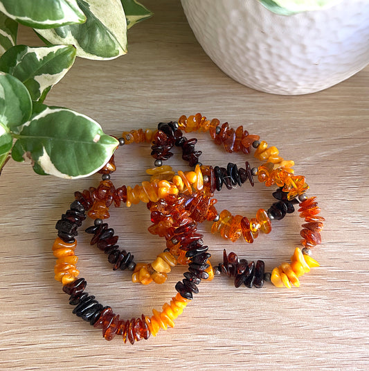 Baltic Amber Bracelets with three colours on a wooden surface with green leaves in the background
