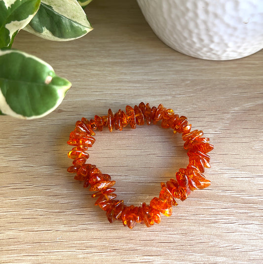 Baltic Amber Chip bracelet on a wooden surface with green leaves and a white textured object in the background.
