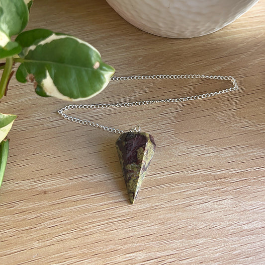 Dragon's Blood pendulum on a wooden surface next to a plant