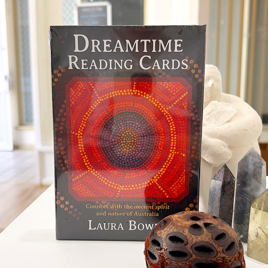Dreamtime Reading Cards by Laura Bowen displayed against a serene background, surrounded by crystals and a natural wooden ornament, showcasing the vibrant Indigenous Australian artwork on the card deck.