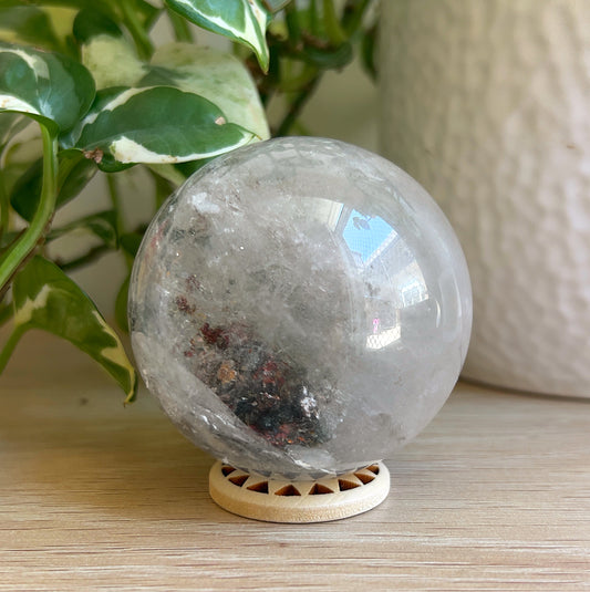 Garden Quartz sphere on wooden stand with plant in background