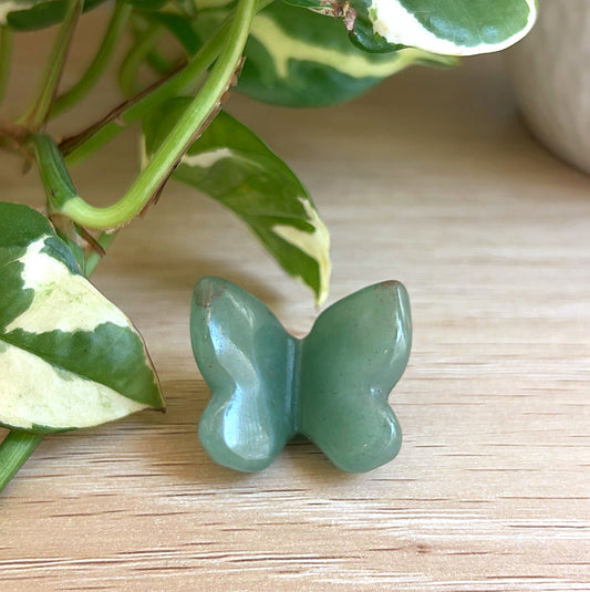Green Aventurine carved butterfly on a wooden surface with leaves in the background