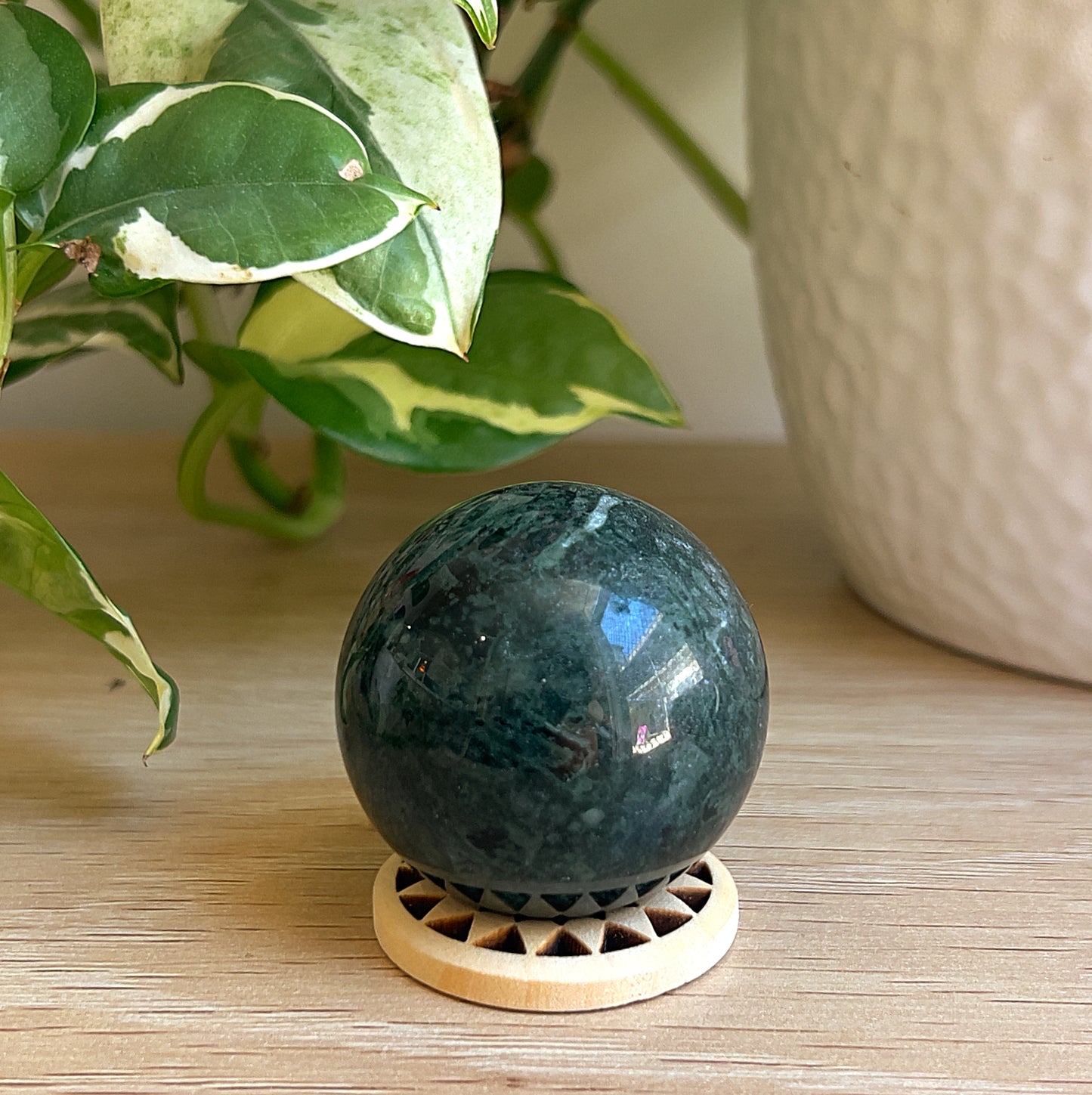 A Kambaba Jasper sphere on wooden sufrace with a plant in the background