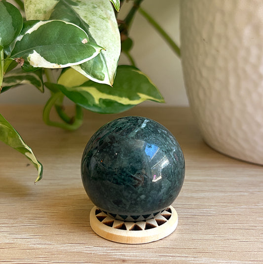 A Kambaba Jasper sphere on wooden sufrace with a plant in the background