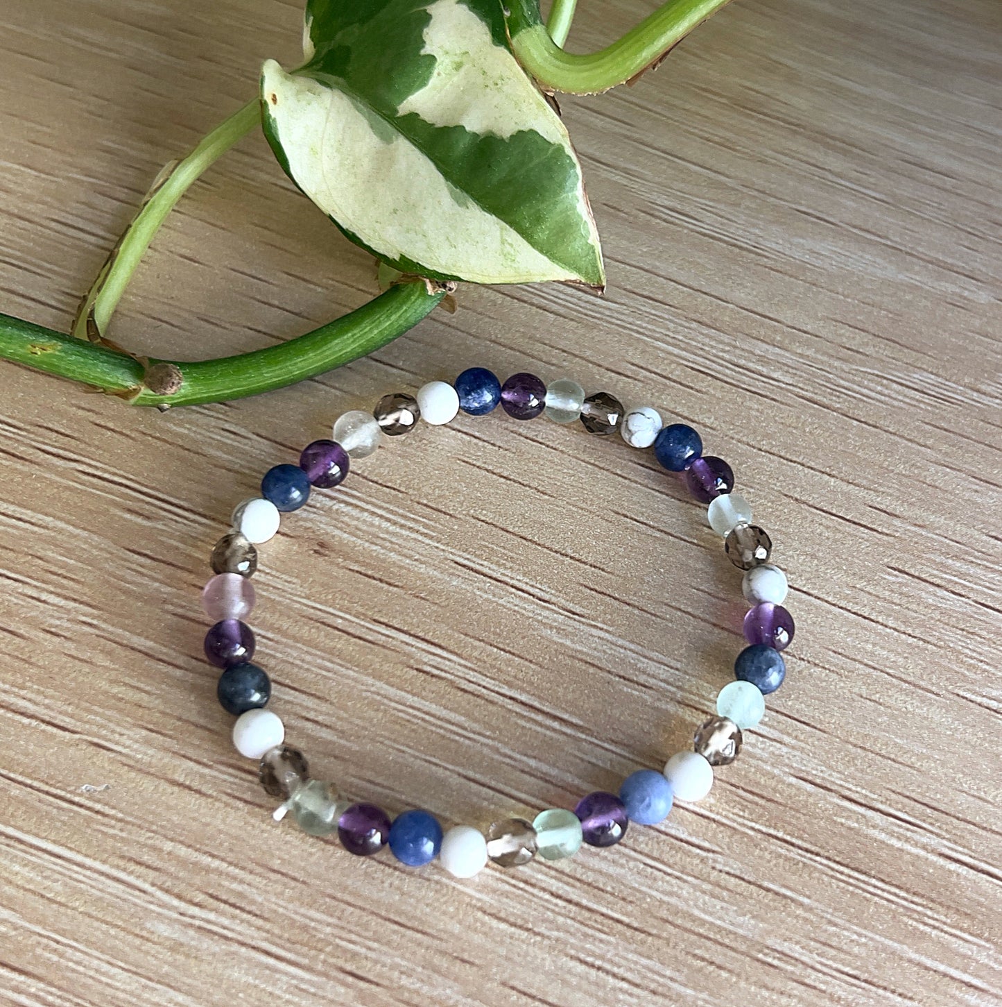 Amethyst, Fluorite, Sodalite, White Howlite, and Smokey Quartz beaded bracelet on a wooden surface with a leafy branch.