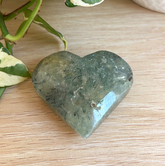 Heart-shaped Prehnite on a wooden surface with a plant in the background