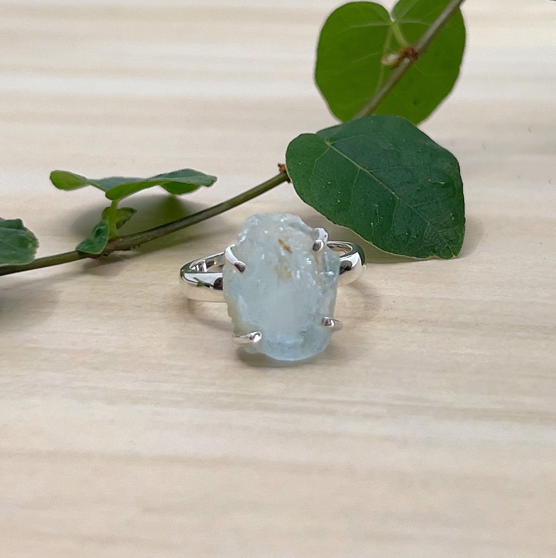Ring with a large, rough-cut Aquamarine gemstone on a wooden surface with leaves.