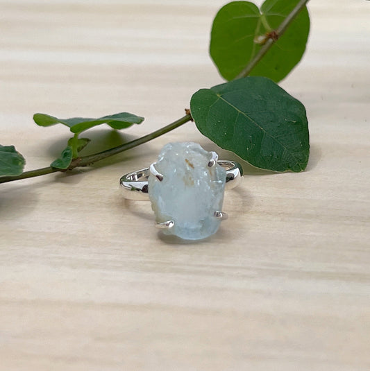 Ring with a large, rough-cut Aquamarine gemstone on a wooden surface with leaves.