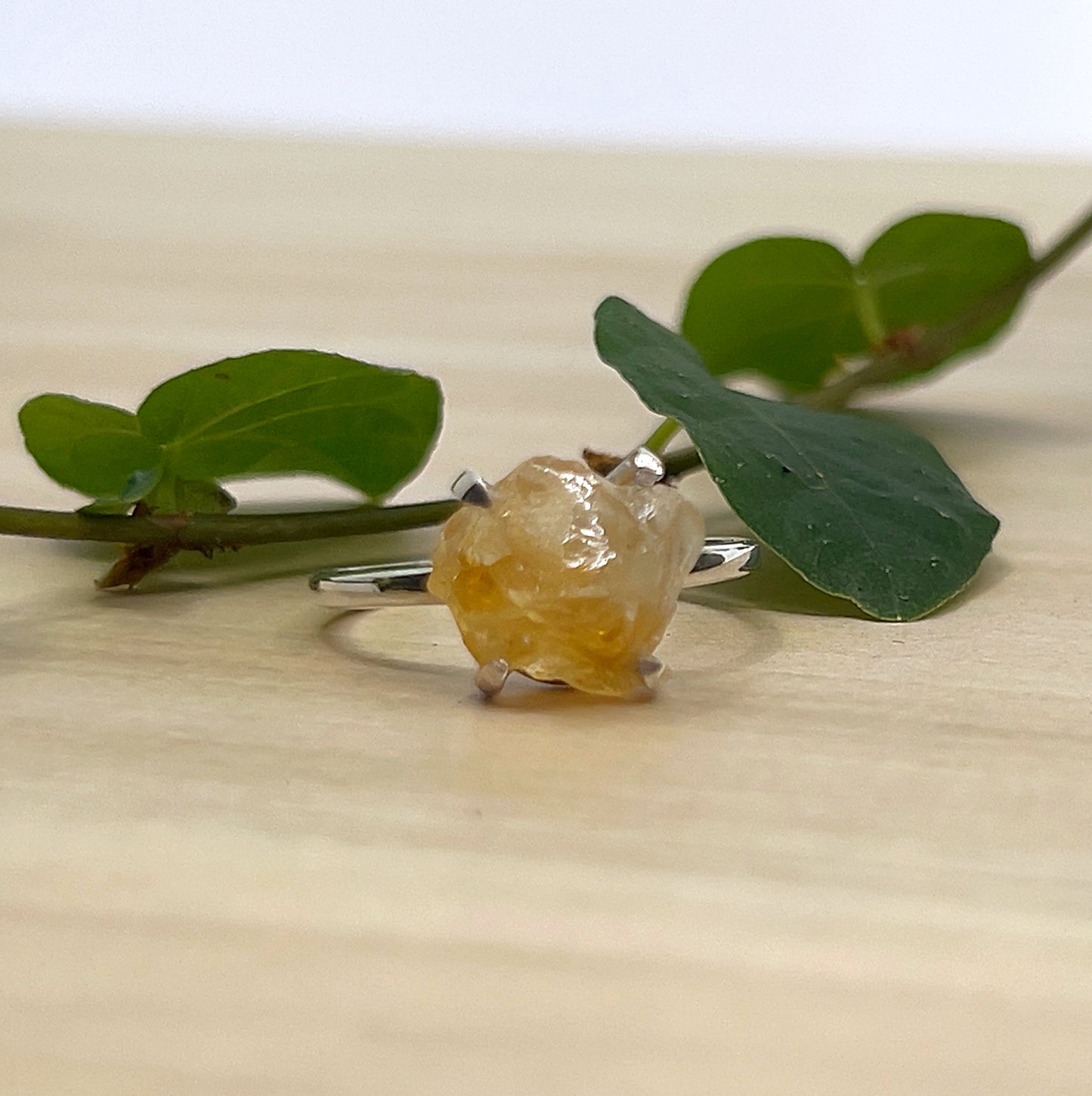 Ring with raw citrine stone on a wooden surface with green leaves