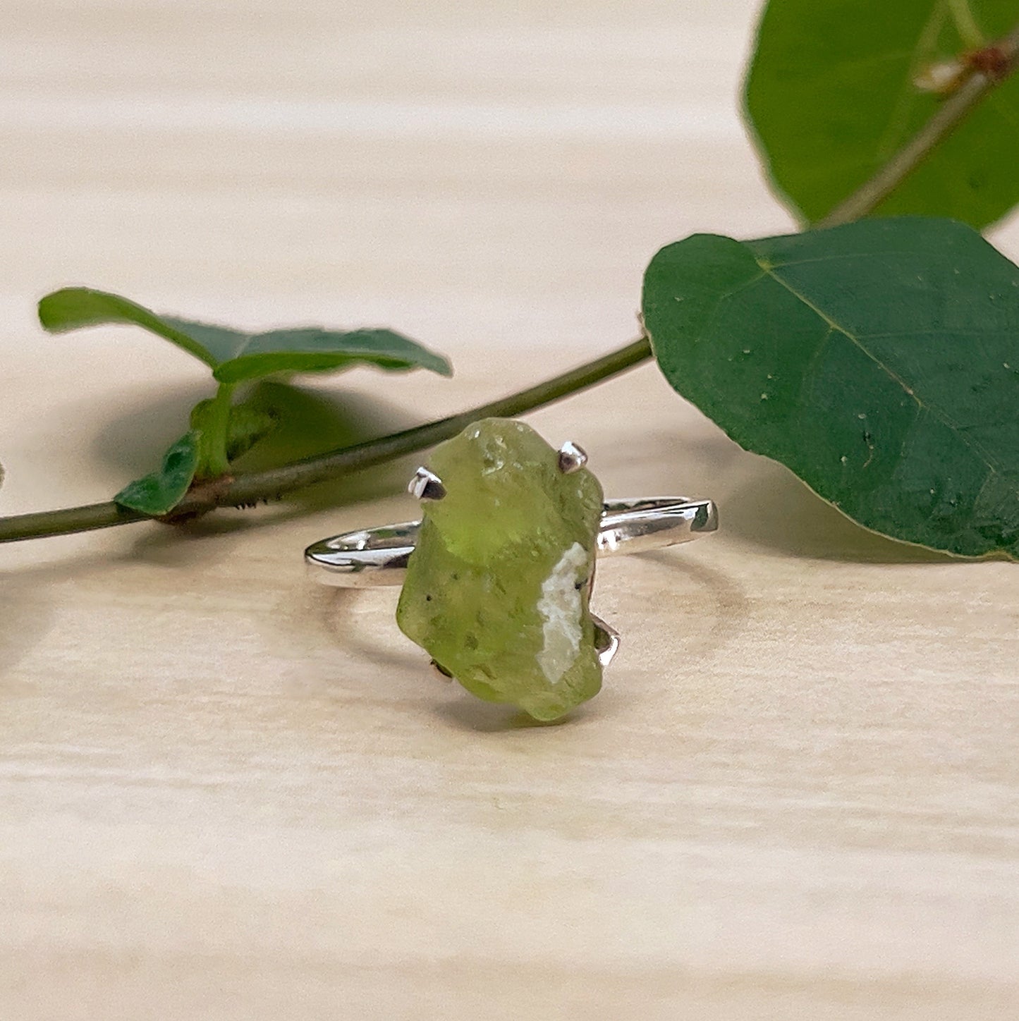 Raw Peridot Ring on wooden surface with green leaves.