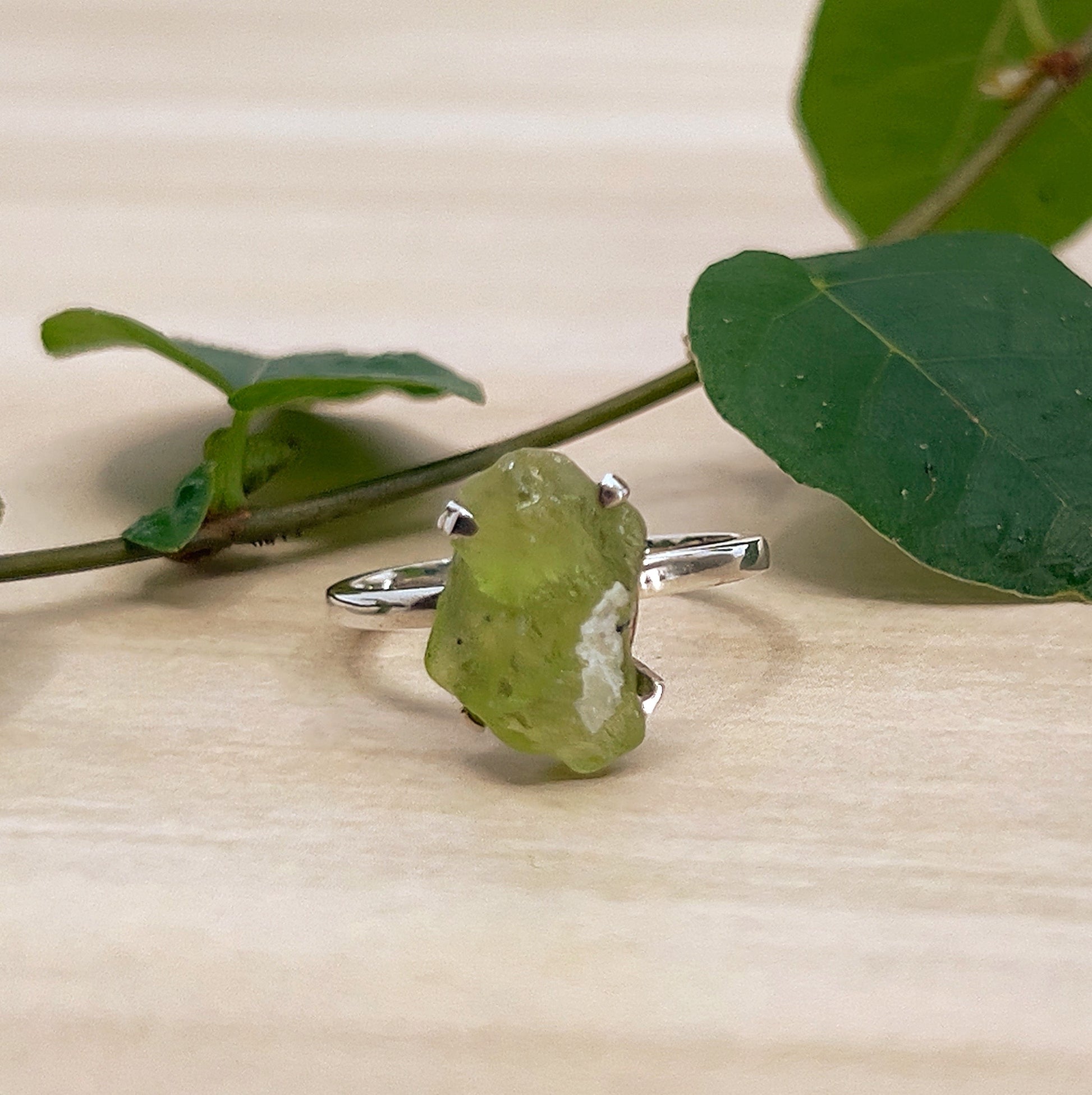 Raw Peridot Ring on wooden surface with green leaves.