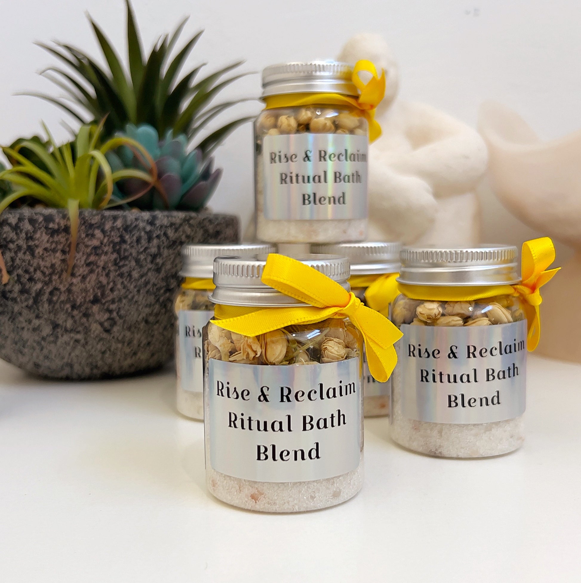 Jars of 'Rise & Reclaim Ritual Bath Blend' with yellow ribbons on a white surface.