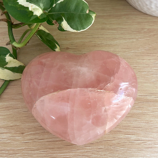 Rose Quartz heart on a wooden surface with green leaves in the background