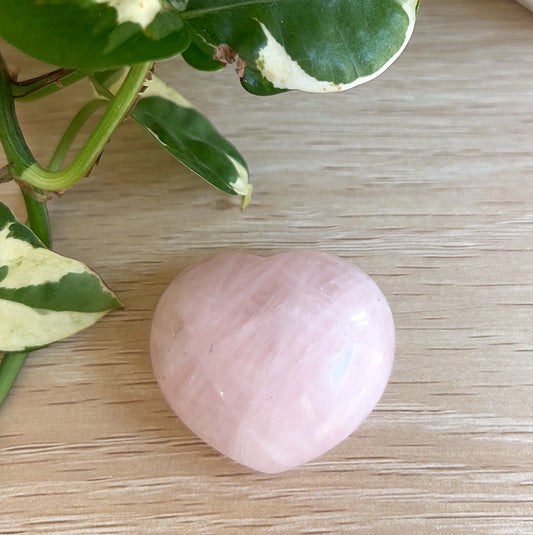Rose Quartz crystal heart on a wooden surface with green leaves