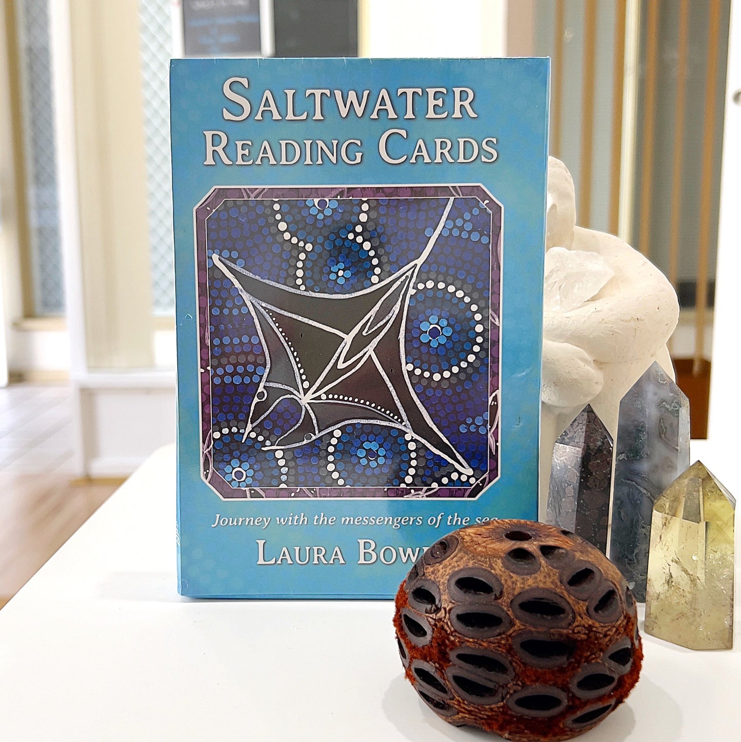 Saltwater Reading Cards by Laura Bowen, featuring a deck of cards with Indigenous Australian artwork of oceanic themes, displayed on a table alongside crystals and natural decor.