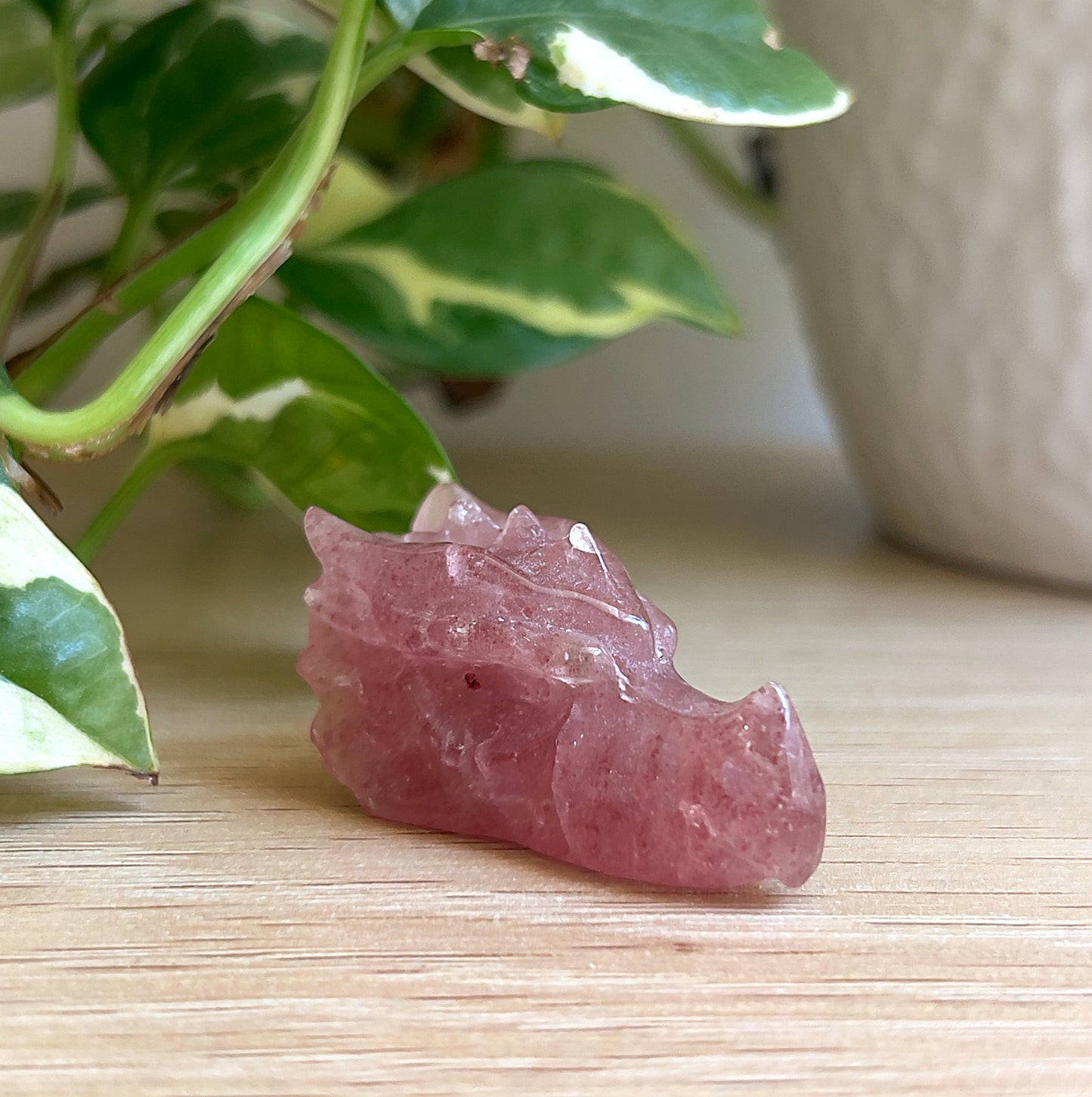 Strawberry Quartz carved dragon head on a wooden surface with green leaves in the background