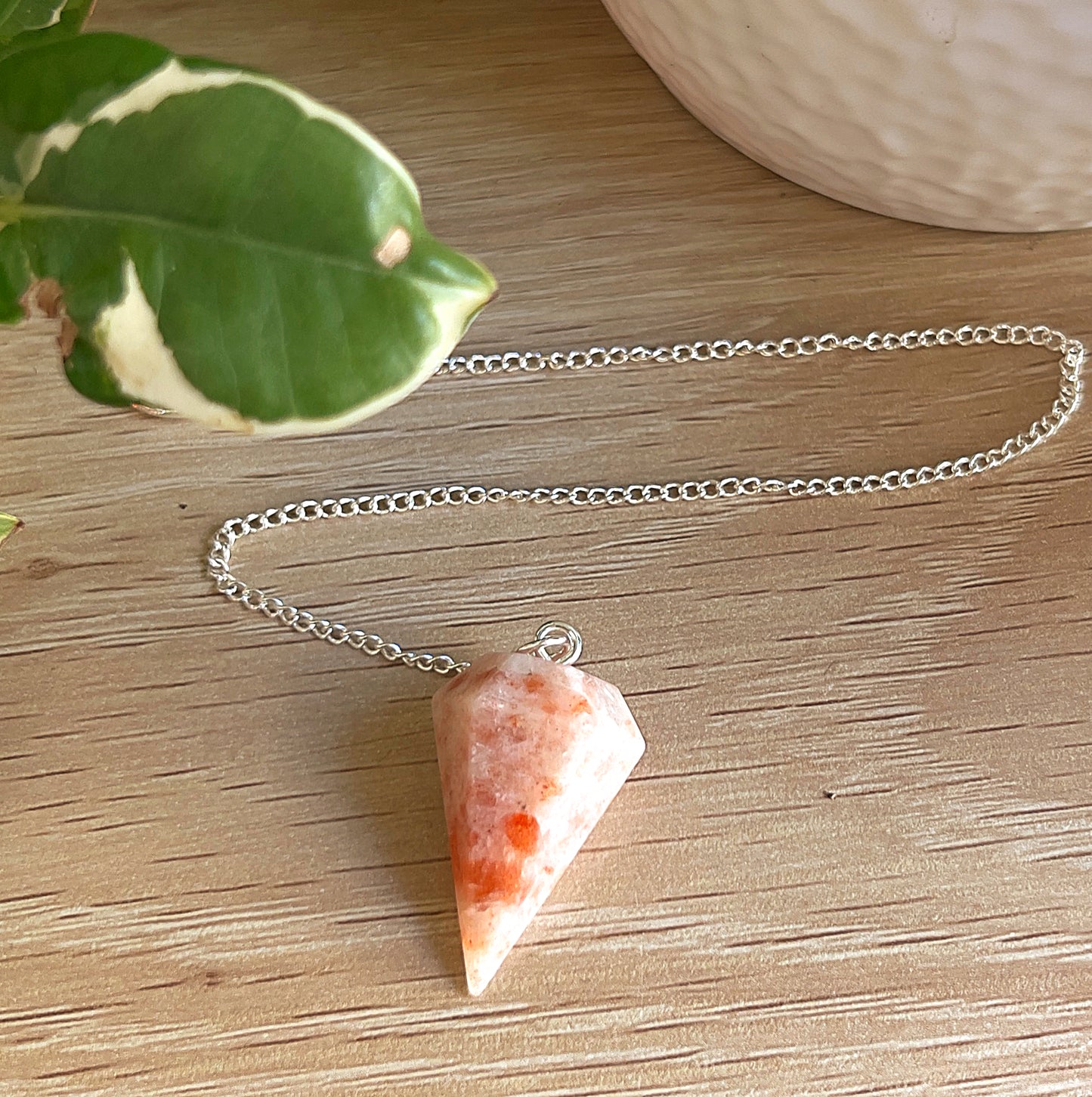 Sunstone pendulum n wooden background with leaf