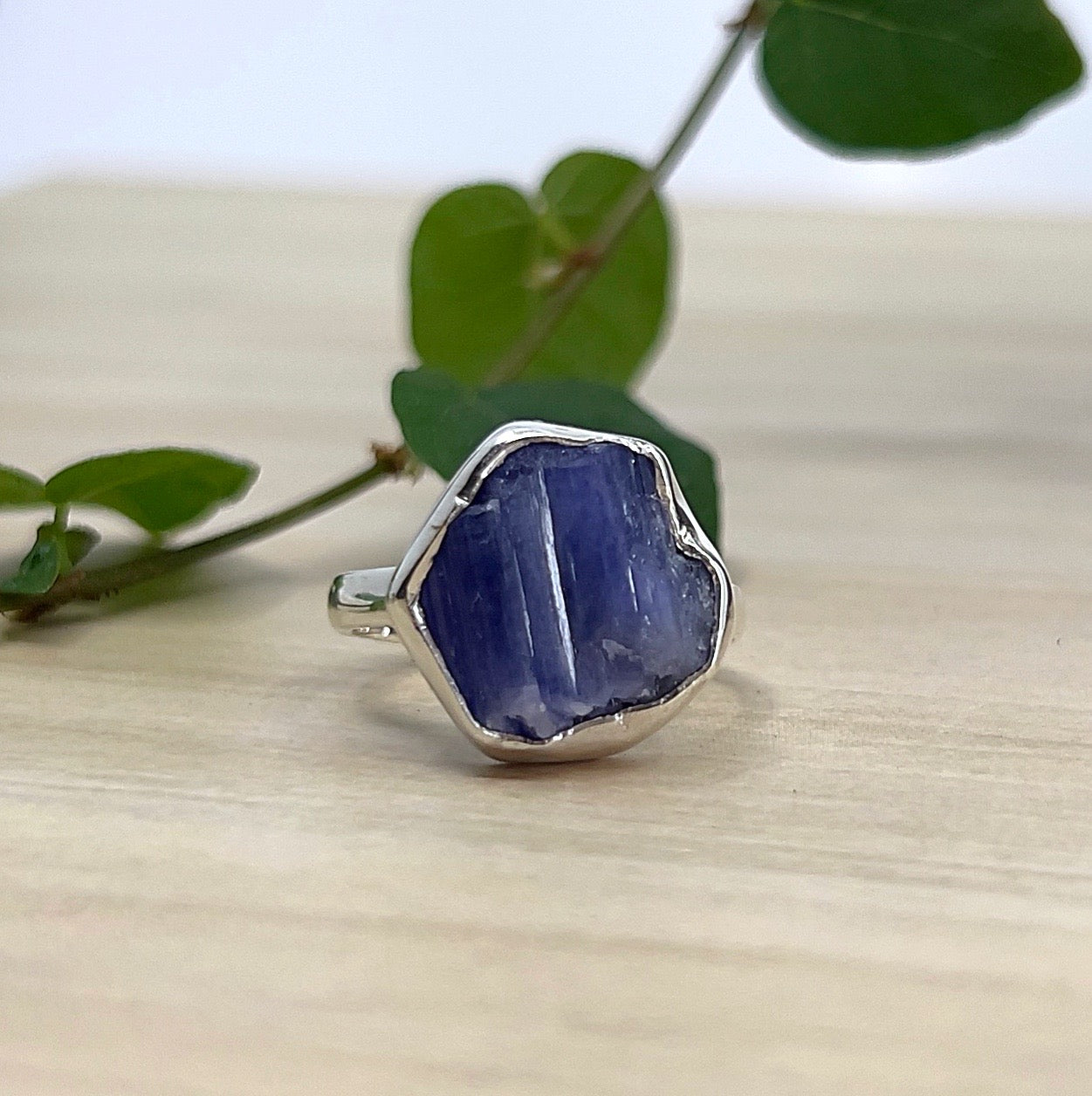 A bezel set raw Tanzanite ring on wooden surfacw with green leaves