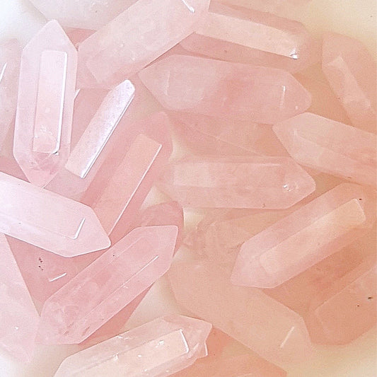 A group of double-terminated rose quartz points spread out on a pale surface, their delicate pink color embodying love and compassion. Each crystal is cut to have a point at both ends, with their translucent quality and soft hue suggesting a gentle, nurturing energy. | Simply Esoteric