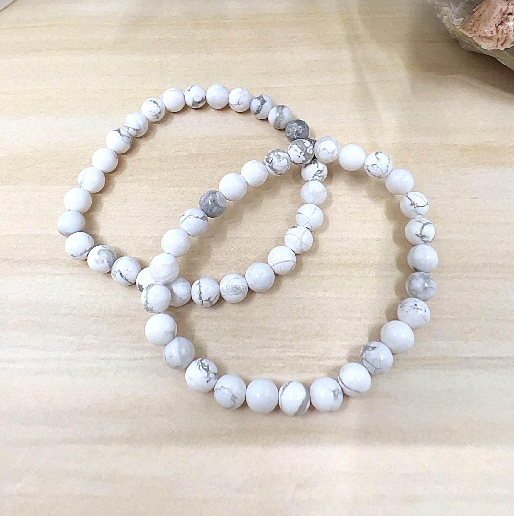 Handmade White Howlite crystal bead bracelet with 6mm round beads on stretchy cord, featuring smooth white stones with natural grey veining, displayed on a wooden surface. | Simply Esoteric