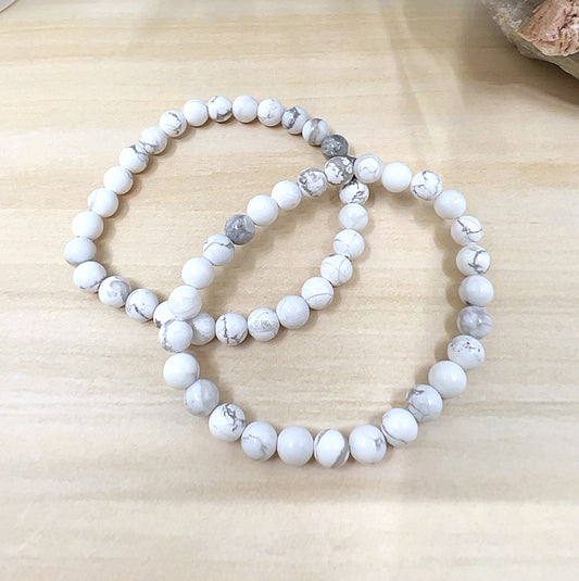 Handmade White Howlite crystal bead bracelet with 6mm round beads on stretchy cord, featuring smooth white stones with natural grey veining, displayed on a wooden surface. | Simply Esoteric