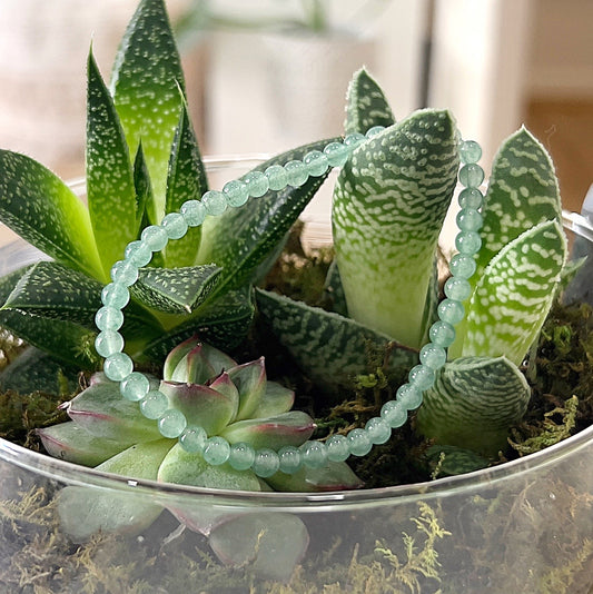 A close-up image of a Green Aventurine bead bracelet, elegantly displayed on a bed of lush green succulents. The bracelet features smooth, round green aventurine beads strung on a stretchy cord, showcasing the natural beauty and calming energy of the stones. | Simply Esoteric