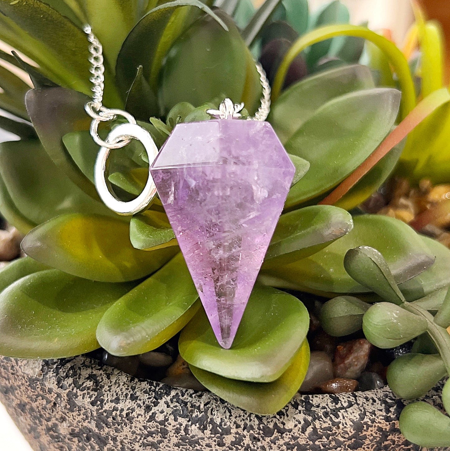 An Amethyst pendulum placed on a background of green succulents. | Simply Esoteric