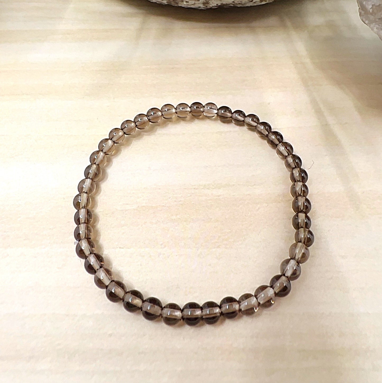 Handmade Smoky Quartz crystal bead bracelet with 4mm round beads on stretchy cord, featuring translucent smoky brown stones, displayed on a wooden surface. | Simply Esoteric