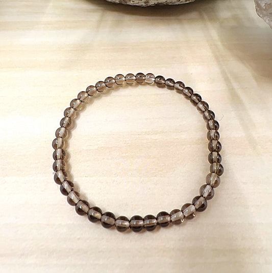 Handmade Smoky Quartz crystal bead bracelet with 4mm round beads on stretchy cord, featuring translucent smoky brown stones, displayed on a wooden surface. | Simply Esoteric