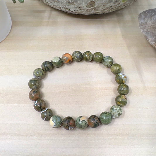 Handmade Rainforest Jasper crystal bead bracelet with 8mm round beads on stretchy cord, featuring earthy green, brown, cream, and orange tones, displayed on a wooden surface. | Simply Esoteric