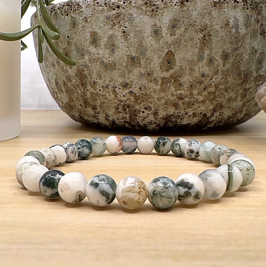Handmade Tree Agate crystal bead bracelet with 6mm round beads on stretchy cord, featuring creamy white and green patterned stones, displayed on a wooden surface. | Simply Esoteric