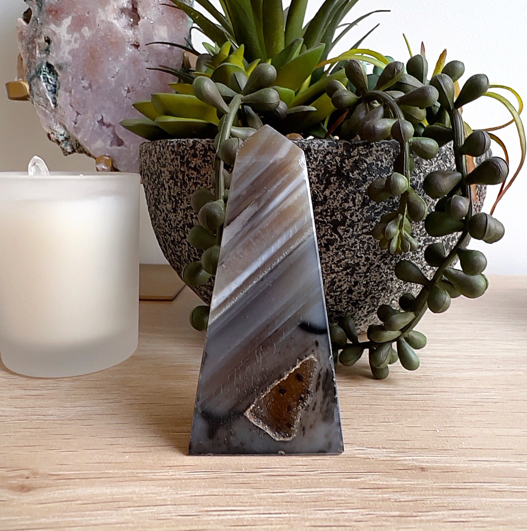 Brown agate obelisk crystal standing upright on a wooden surface, displaying layered natural brown and grey banding with a geode-like pocket at the base. | Simply Esoteric