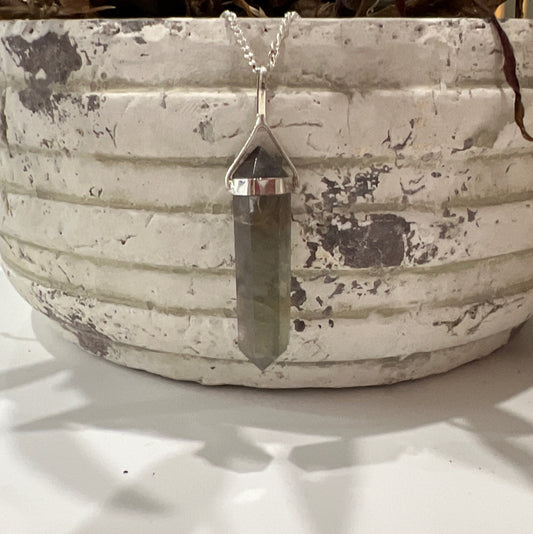 A double terminated fluorite pendant with green and yellow hues, set in sterling silver, displayed against a rustic background | Simply Esoteric