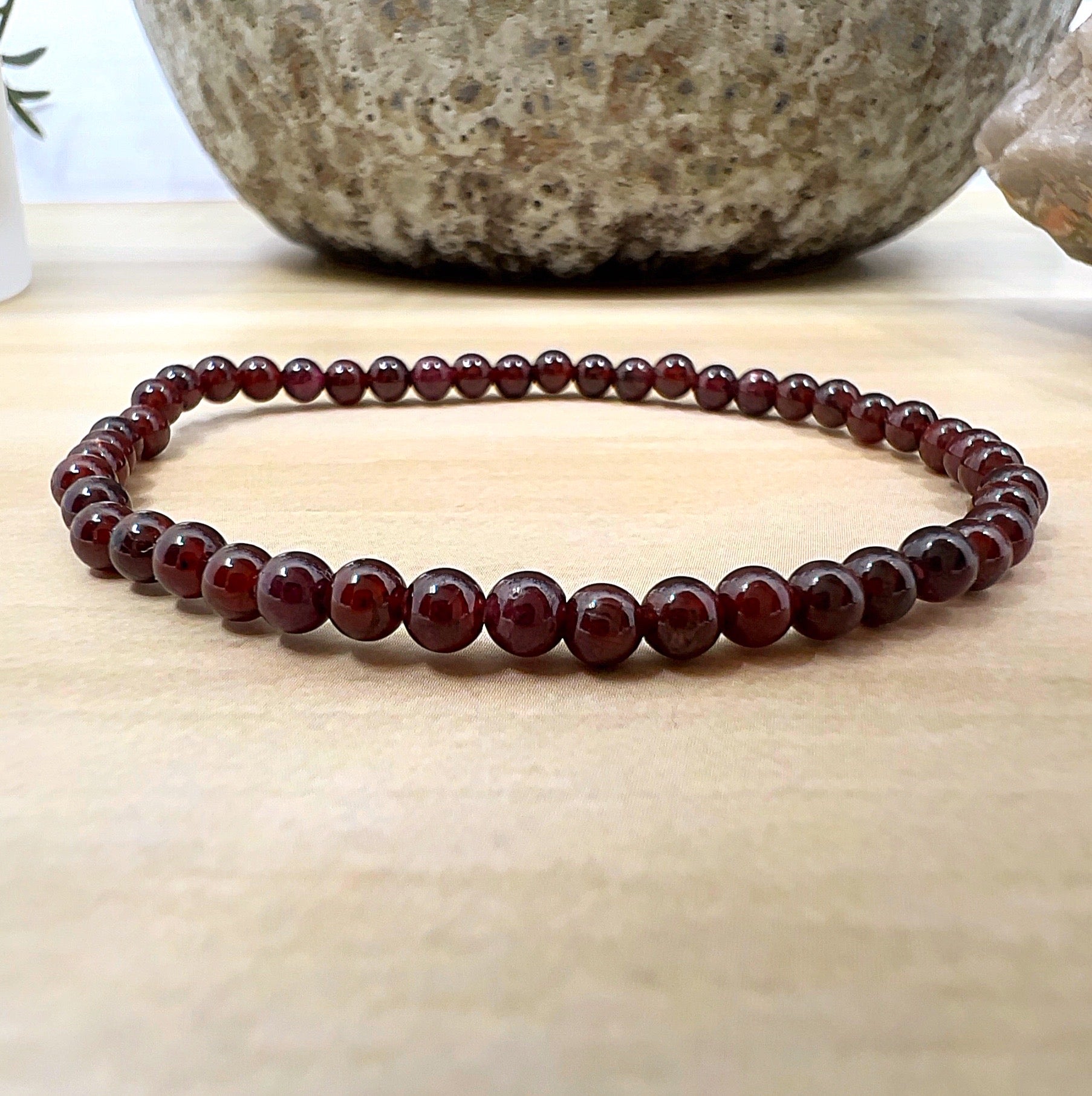 Handmade Garnet crystal bead bracelet with 4mm round beads on stretchy cord, featuring deep red polished stones, displayed on a wooden surface. | Simply Esoteric